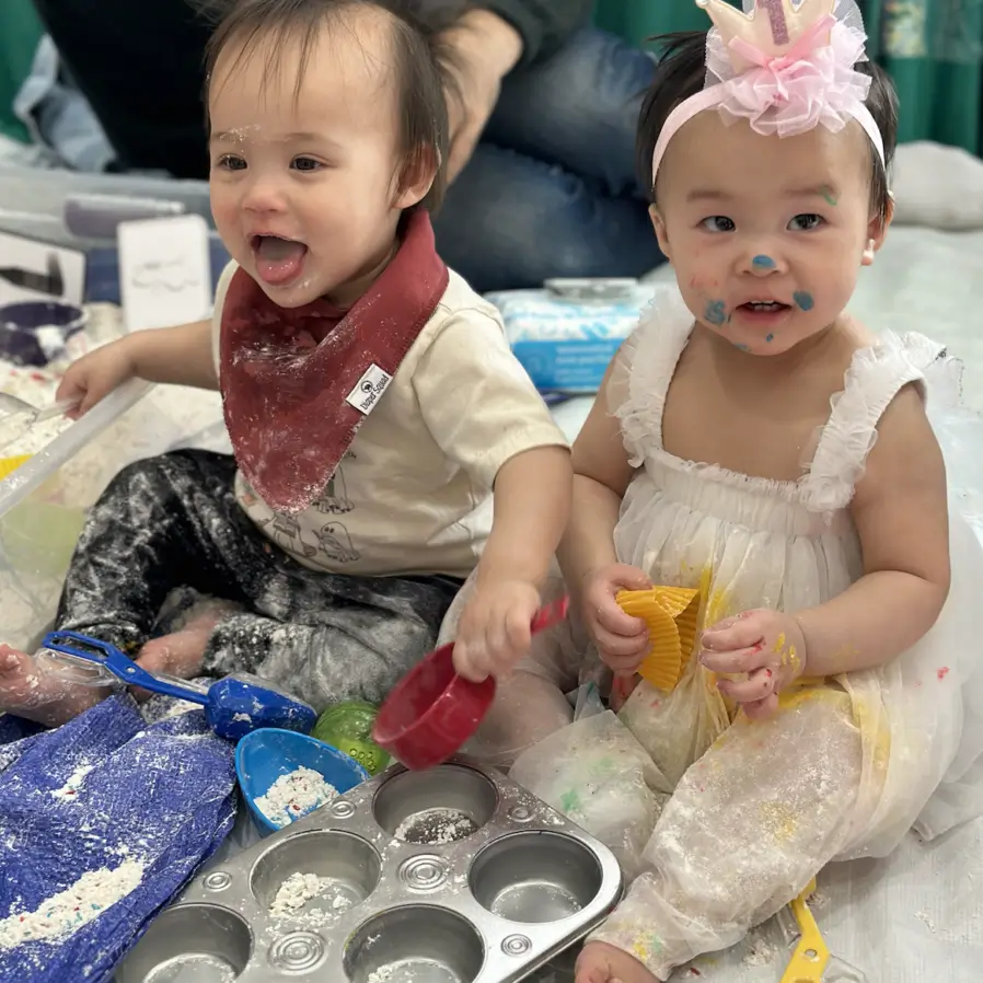 Two toddlers enjoying a messy play session with flour and baking tools.